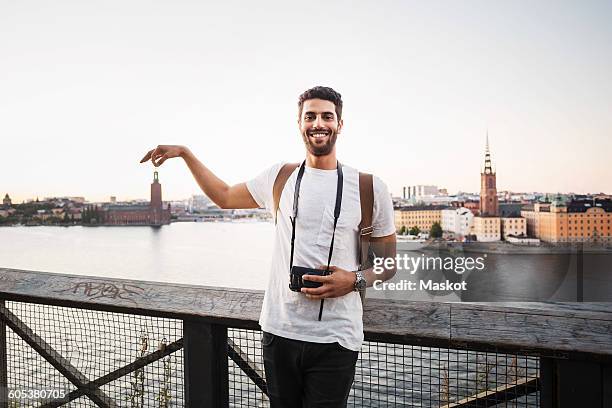 optical illusion of happy male tourist holding building in city against clear sky - optische illusion stock-fotos und bilder