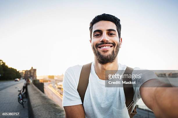 portrait of happy male tourist sitting on retaining wall of bridge - jeunes hommes photos et images de collection