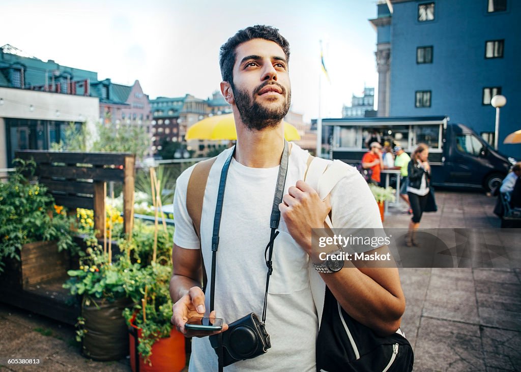 Tourist looking away while holding smart phone during vacation