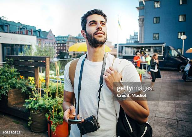 tourist looking away while holding smart phone during vacation - tourist fotografías e imágenes de stock