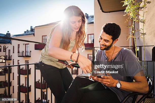 happy couple using smart phone while reading guidebook on balcony - letting it all hang out stock pictures, royalty-free photos & images