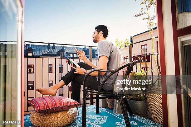 side view of man holding smart phone and guidebook while looking away at balcony - balcony reading stock pictures, royalty-free photos & images