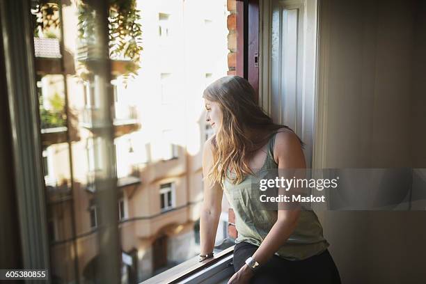 young woman looking through window at home - arrendatario fotografías e imágenes de stock