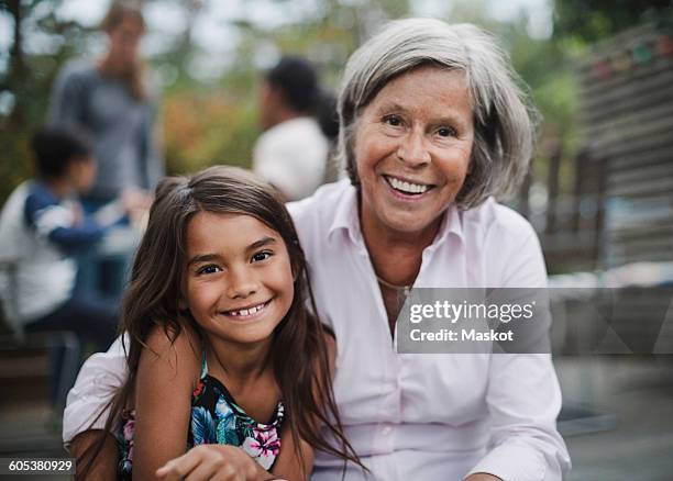 portrait of happy grandmother sitting with granddaughter at yard - granddaughter stockfoto's en -beelden