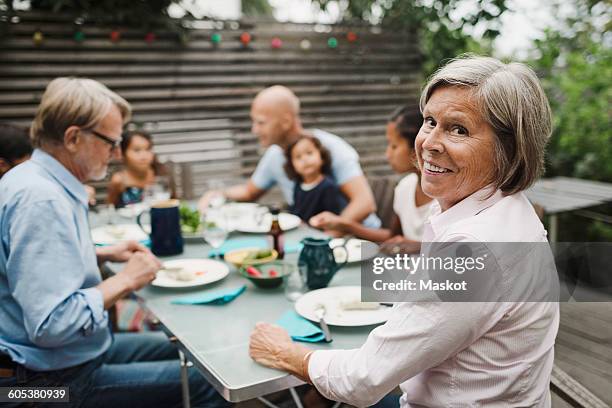 portrait of happy senior woman sitting with family at outdoor dining table - sogra imagens e fotografias de stock