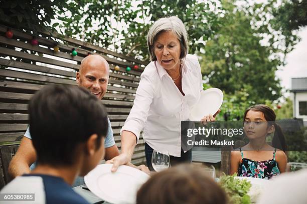 senior woman giving plate to grandson at outdoor dining table - dinner on the deck stock pictures, royalty-free photos & images