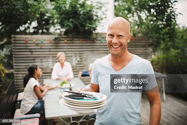 portrait of happy man holding plates with family sitting at outdoor table in yard - mid aged stock pictures, royalty-free photos & images