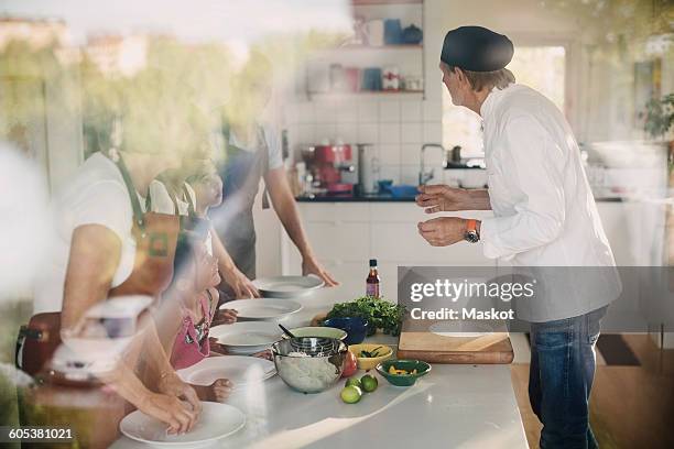 senior man in chefs jacket guiding family in preparing asian food at kitchen - chef coat stock pictures, royalty-free photos & images