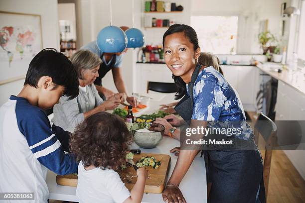 portrait of happy woman standing with family preparing food at table in kitchen - ritratto nonna cucina foto e immagini stock