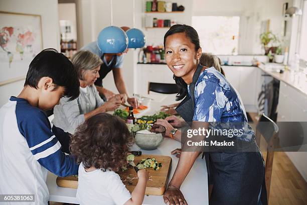 portrait of happy woman standing with family preparing food at table in kitchen - yellow bell pepper stock pictures, royalty-free photos & images