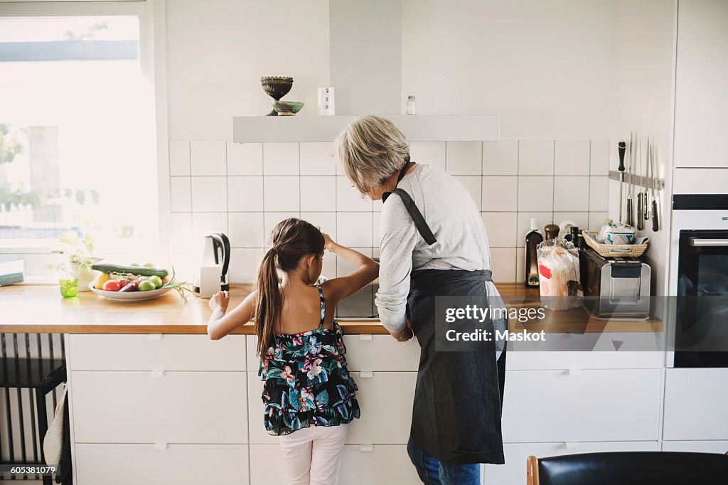 Rear view of girl standing with grandmother preparing food in kitchen