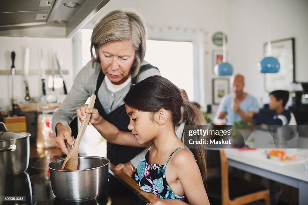 Grandmother looking at girl cooking at kitchen counter