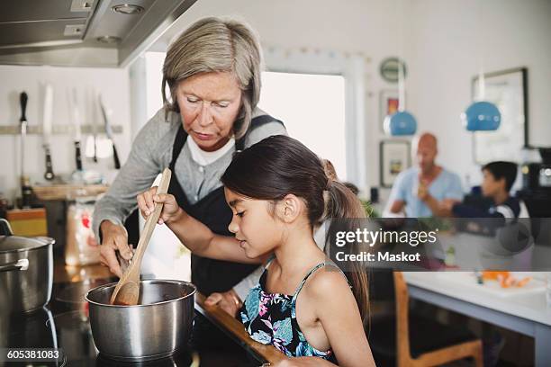 grandmother looking at girl cooking at kitchen counter - mother daughter cooking stock pictures, royalty-free photos & images