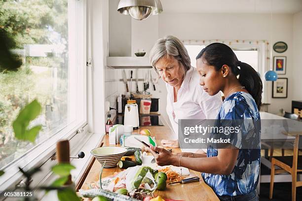 senior woman using digital tablet with daughter-in-law while cooking food in kitchen - schoondochter stockfoto's en -beelden