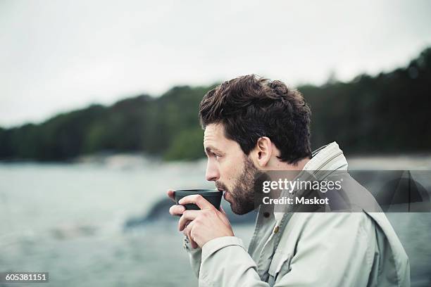 side view of man drinking coffee at sea shore - sea cup stock pictures, royalty-free photos & images