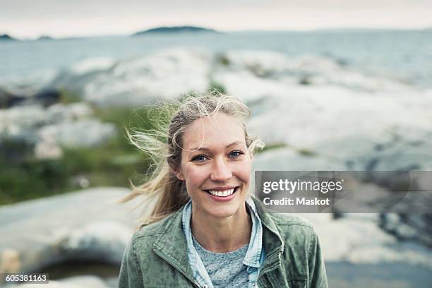 portrait of happy young woman on rock by sea - young blonde woman facing away photos et images de collection