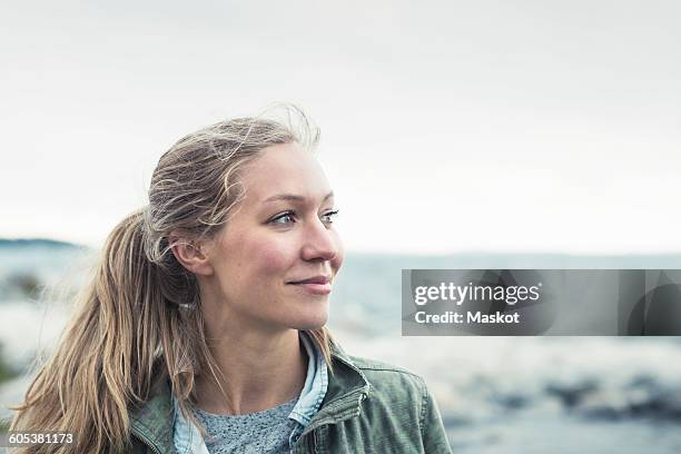 smiling young woman looking away by sea against sky - kvinna and norden bildbanksfoton och bilder