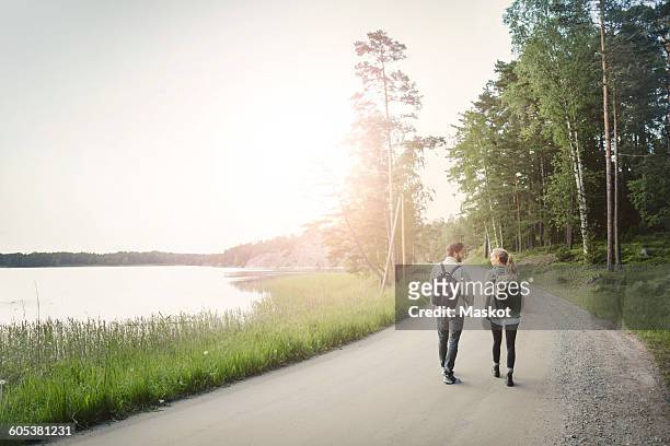 rear view of wonderlust couple walking on road by lake against clear sky - walking side view stock-fotos und bilder