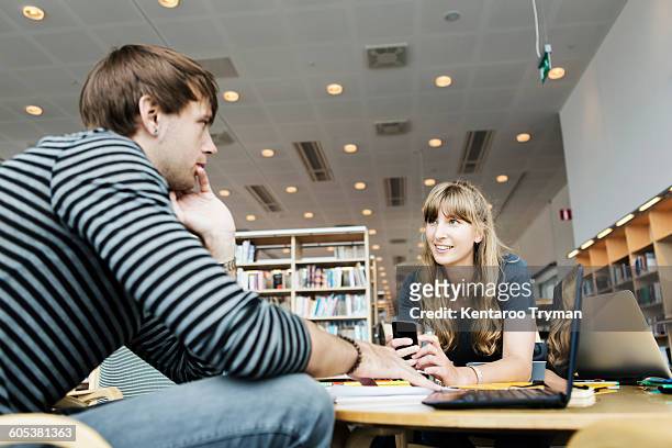 young woman with male friend discussing at table in college library - college student holding books stockfoto's en -beelden