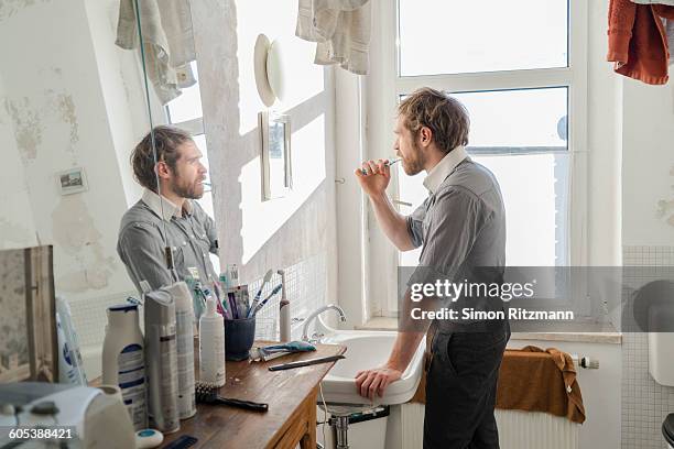 young man brushing teeth in bathroom - side view mirror stockfoto's en -beelden