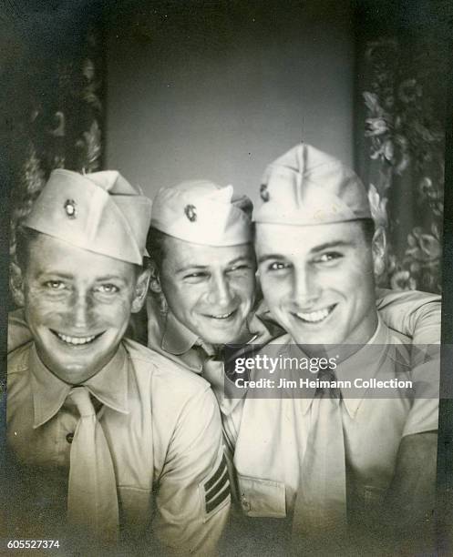 Three men in uniform crowded into tight space for photobooth picture.