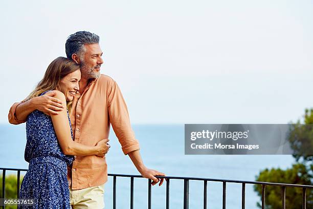 couple embracing by railing while looking at sea - mature adult couple stock-fotos und bilder