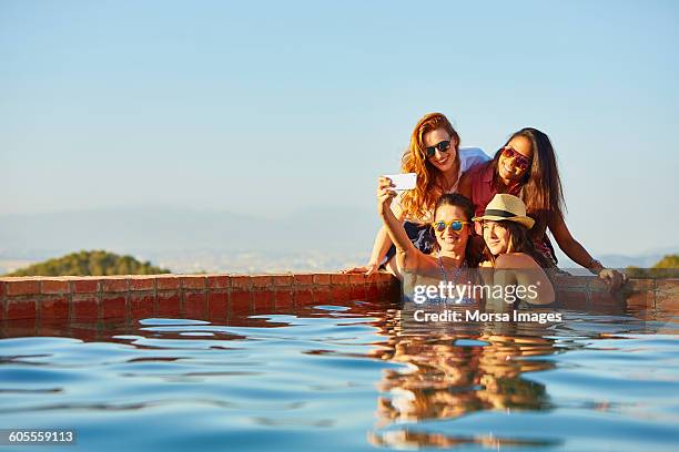 female friends taking self portrait at pool's edge - mobile phones group stockfoto's en -beelden