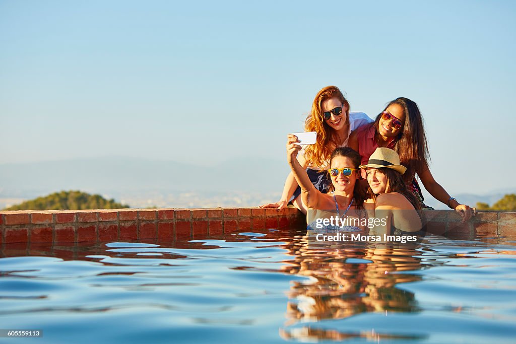 Female friends taking self portrait at pool's edge