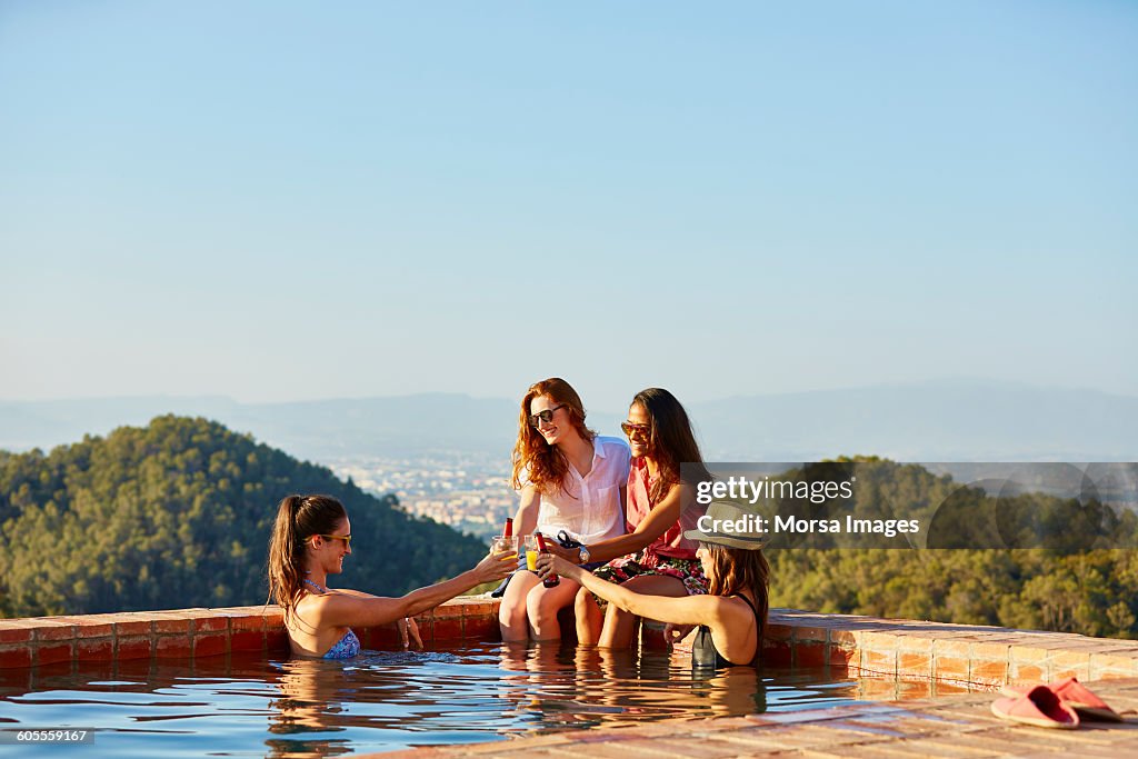 Female friends toasting drinks at pool's edge