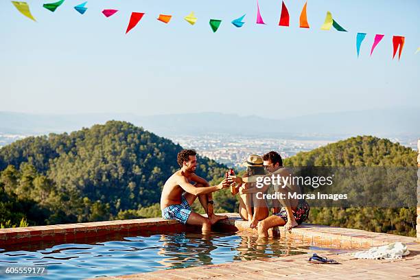 friends toasting beer bottles at pool's edge - piscine de complexe balnéaire photos et images de collection