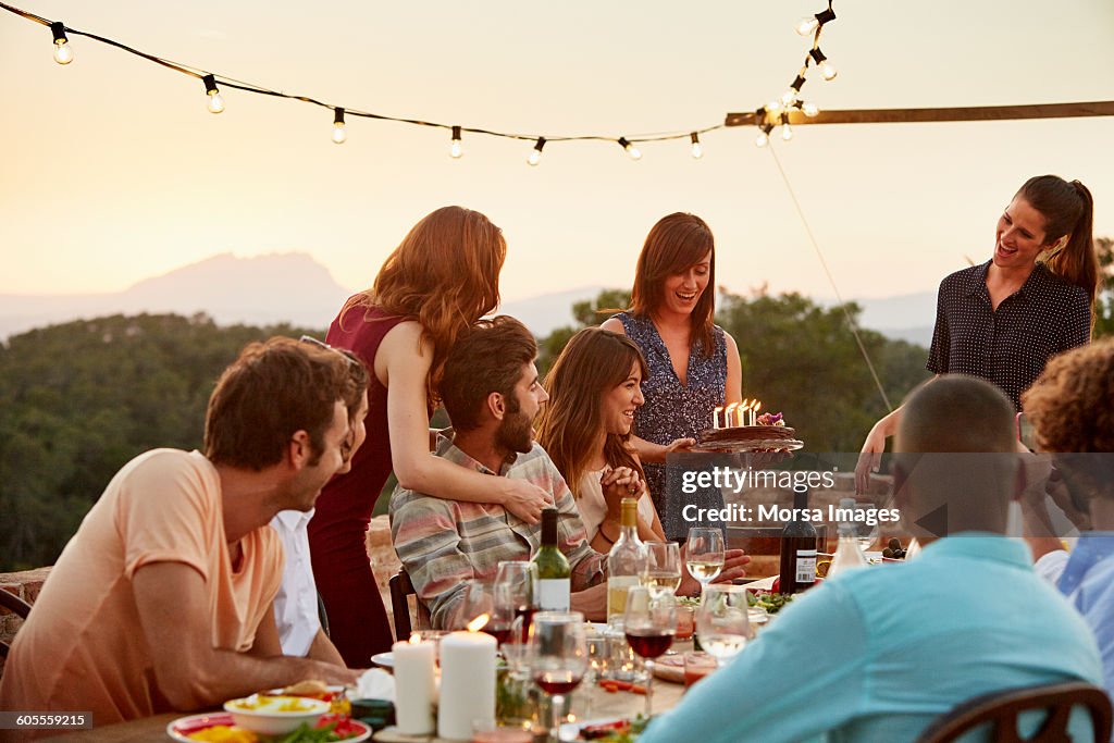 Woman carrying cake by friends at table