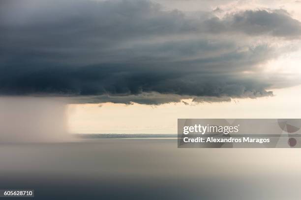 dramatic thunder cloud with rain shaft over the ocean - alexandros maragos stock pictures, royalty-free photos & images