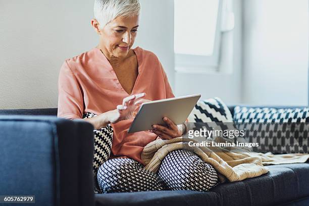 older caucasian woman using digital tablet on sofa - science and technology ebook stock pictures, royalty-free photos & images