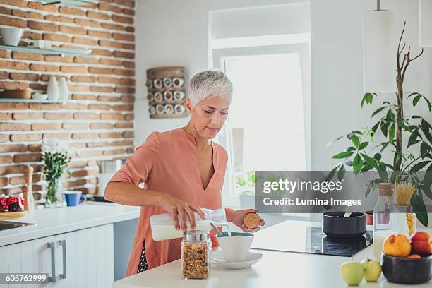older caucasian woman pouring milk in kitchen - une seule femme d'âge mûr photos et images de collection