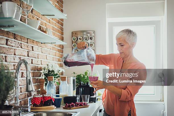 older caucasian woman pouring smoothie in kitchen - mature woman smoothie stock-fotos und bilder