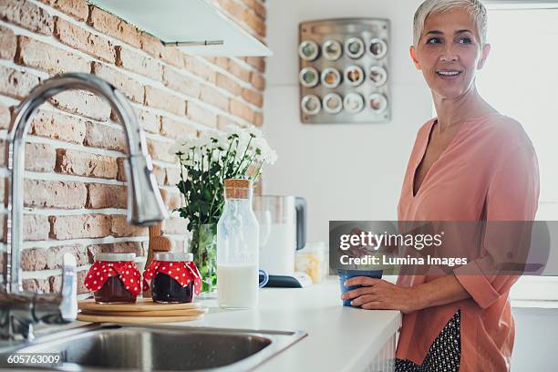 older caucasian woman stirring coffee in kitchen - stirring stock pictures, royalty-free photos & images