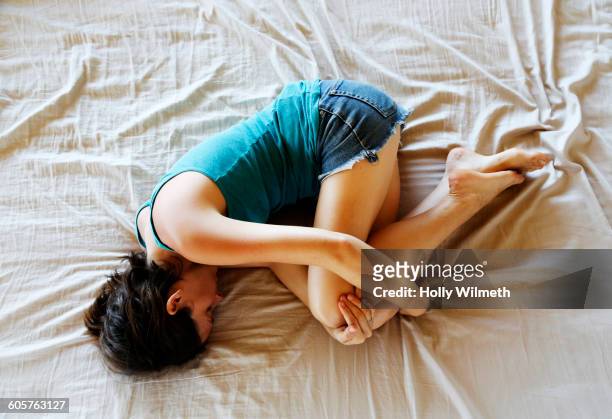 woman curled in fetal position on bed - position du foetus photos et images de collection