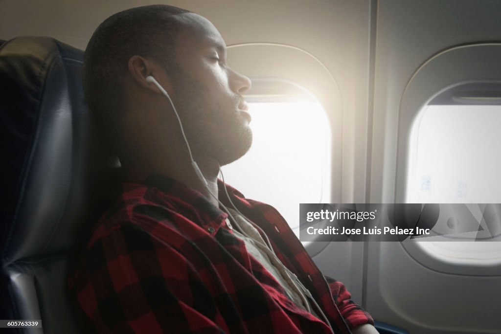 Black man listening to earbuds on airplane
