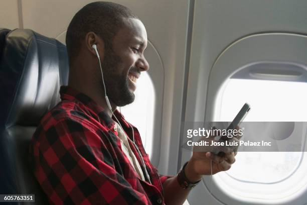 black man listening to earbuds on airplane - phone mid air stock pictures, royalty-free photos & images