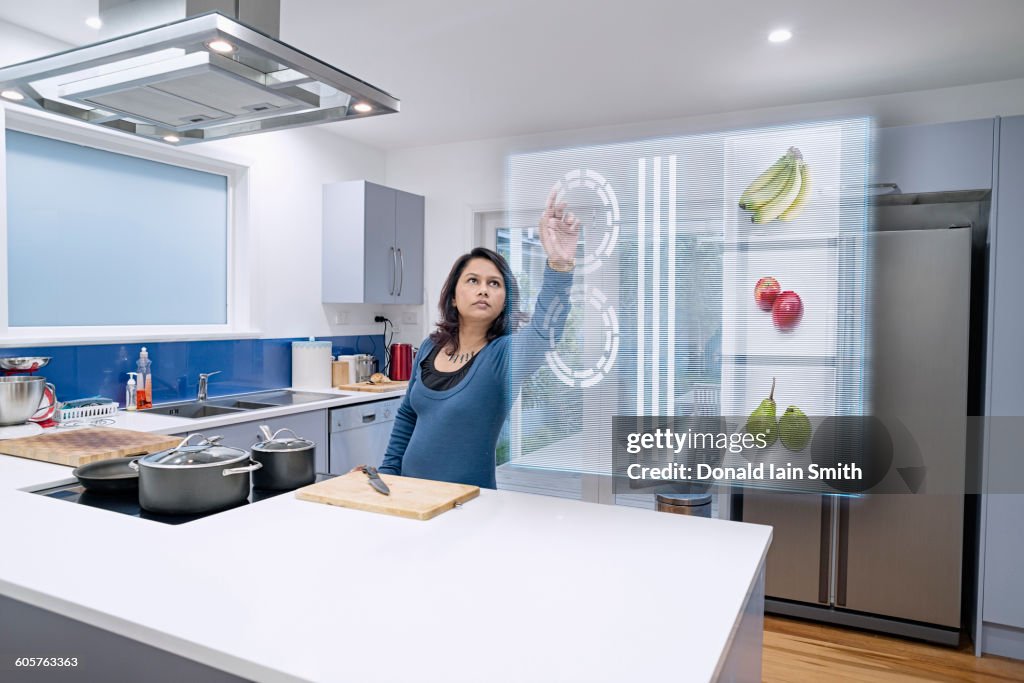 Mixed race woman using holographic screen in kitchen