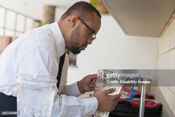 mixed race server with down syndrome filling pitcher in restaurant - henkelkrug stock-fotos und bilder