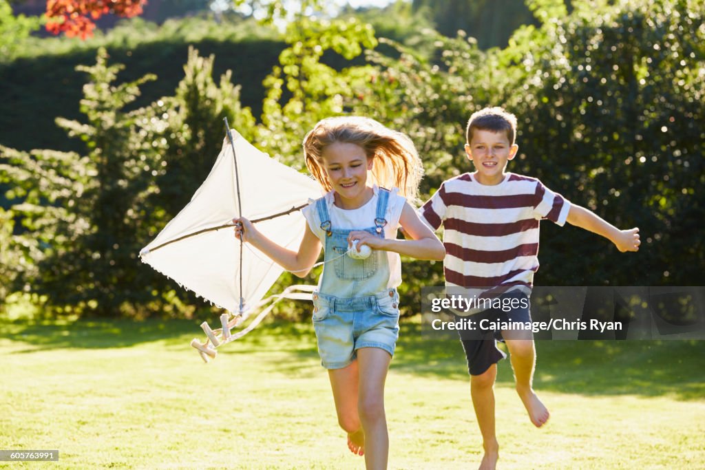 Bruder und Schwester laufen mit Drachen im sonnigen Garten