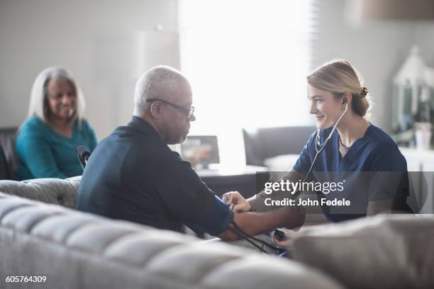 nurse taking patient blood pressure in living room - medical examination room stockfoto's en -beelden