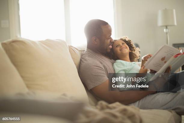 father and daughter reading on sofa - african american dad stock-fotos und bilder