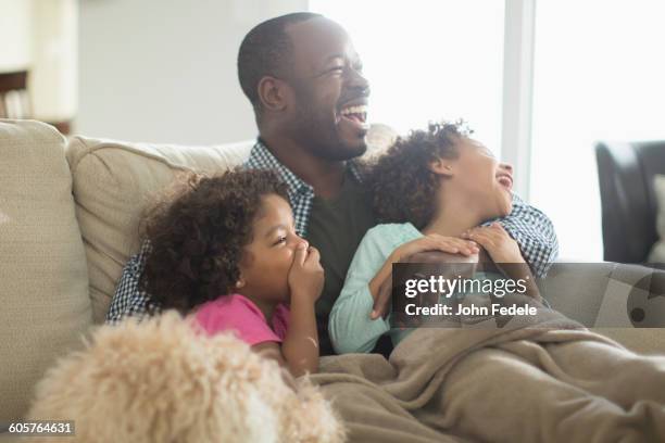 father and daughters watching television on sofa - family tv stock-fotos und bilder