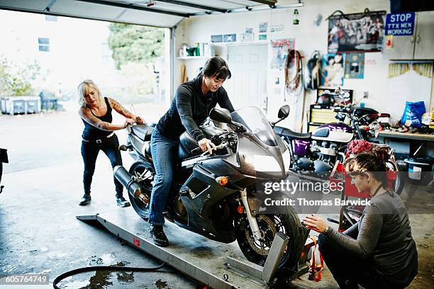 female mechanics loading motorcycle on lift - partnership men bikes stockfoto's en -beelden