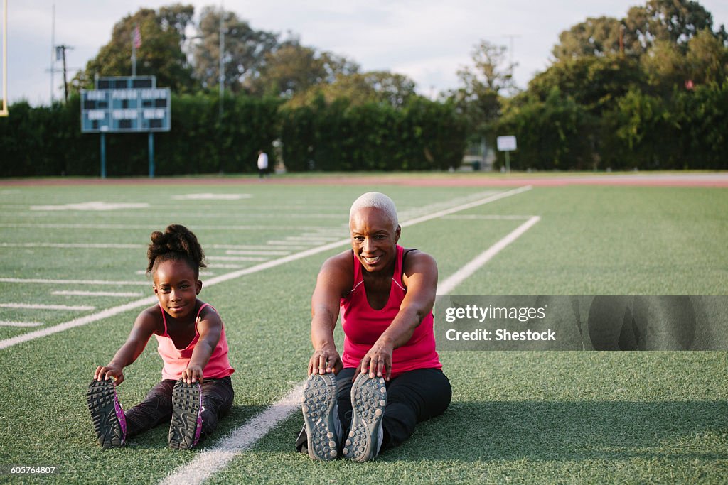 Grandmother and granddaughter stretching on football field