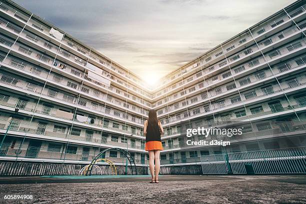 the rear view of woman standing against old apartment building, looking towards the sun shining - apartamento municipal imagens e fotografias de stock