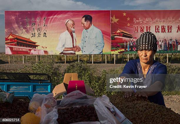 An ethnic Uyghur woman arranges raisins for sale at her stall with a billboard showing the late Communist Party leader Mao Zedong in the background...