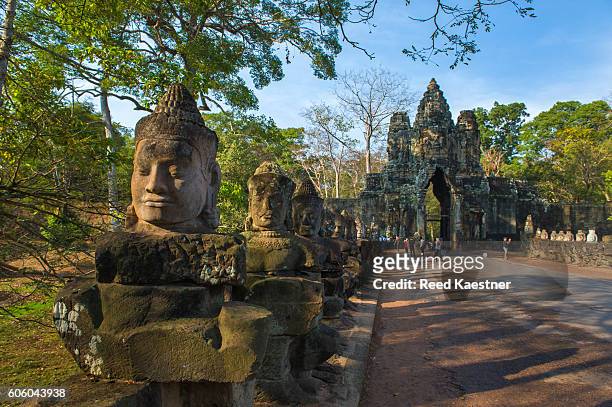 carved heads line the road way to the gated entrance to angkor thom and the bayon temple at angkor wat, siem reap, cambodia - angkor thom fotografías e imágenes de stock